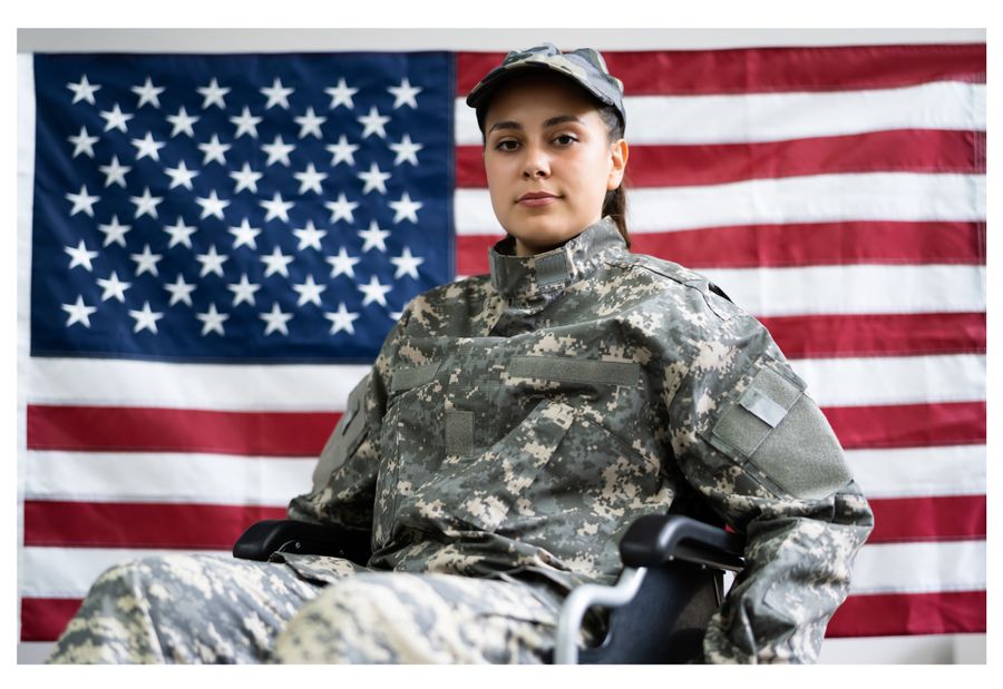 A young woman veteran in uniform, seated in front of the American flag
