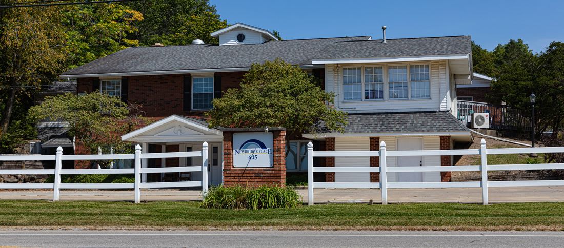Newbridge Place at 645 Wooster Street — a brick home with a white rail fence and the Newbridge Place sign