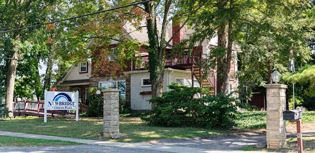 Newbridge Veterans Place — a tree-shaded home with stone pillars, an accessibility ramp, and the Veterans Place sign